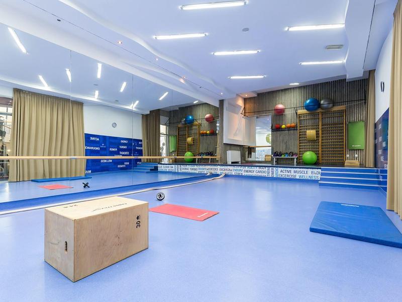 Salle de sport moderne avec sol bleu, mur miroir, aides à l'exercice et caisse en bois.