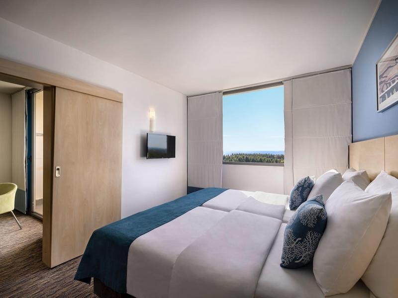 Chambre d'hôtel moderne avec lit double, télévision et porte coulissante ouverte vers une autre pièce.