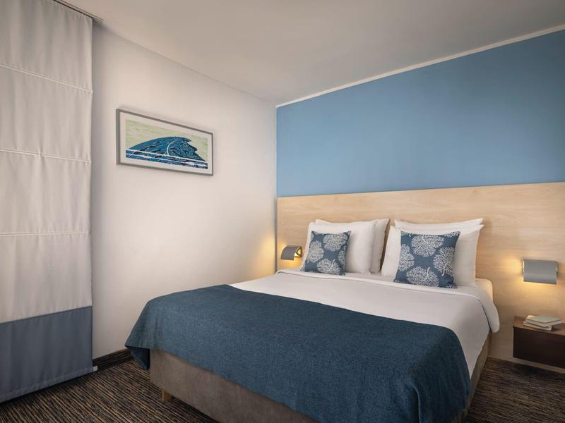 Chambre d'hôtel moderne avec lit double, accents bleus et décoration murale minimaliste.