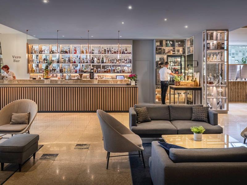 Salon d'hôtel moderne avec fauteuils confortables, canapés et bar en arrière-plan.