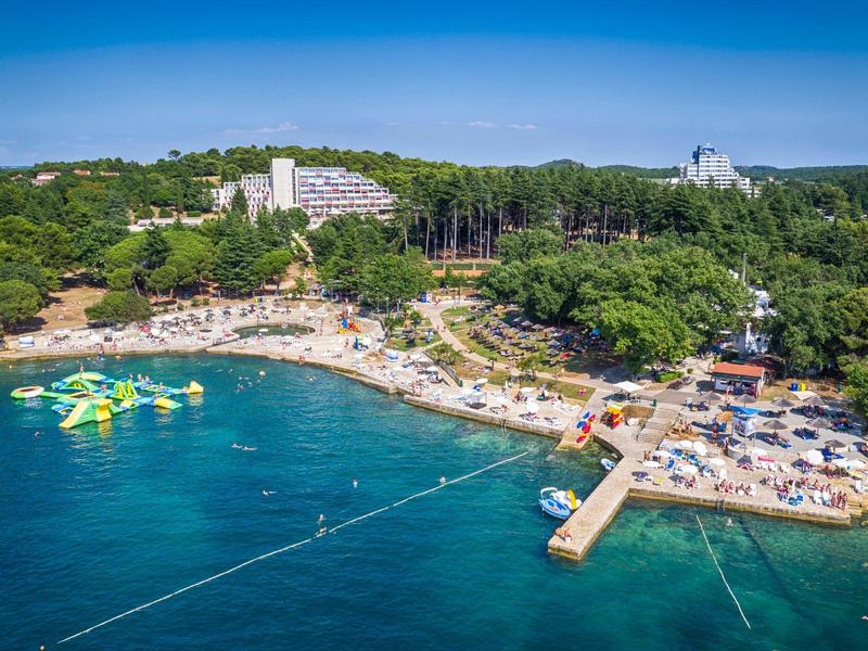 Plage avec transats, grand hôtel en arrière-plan et parc aquatique gonflable dans la mer.
