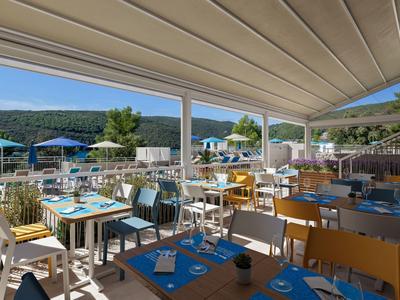 Terras van een restaurant met gedekte tafels en een blauwe hemel in een vakantiegebied.