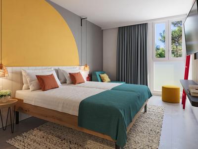 Modern hotelkamer met tweepersoonsbed, gele wandontwerp, tapijt en uitzicht via het raam.