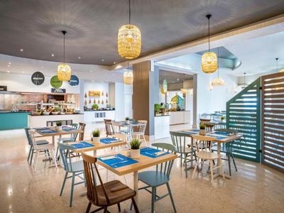 Modern hotelrestaurant met houten stoelen, gedekte tafels en hanglampen.