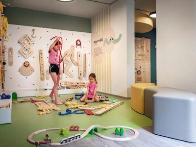 Kinderen spelen op een groen tapijt met houten trein in een lichte hotel speelkamer.