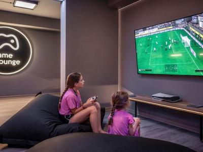 Twee meisjes zitten op zitzakken in een kamer en kijken naar voetbal op een groot tv-scherm.