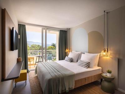 Moderne hotelkamer met tweepersoonsbed, balkon en uitzicht op de natuur.