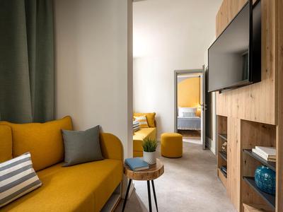 Gezellige woonruimte met gele bank, houten meubels en uitzicht op een aangrenzende slaapkamer.