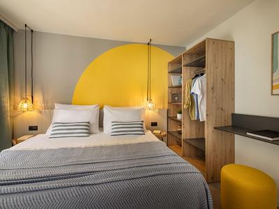 Moderne hotelkamer met twee bedden, gele halve cirkel op de muur en houten kast.