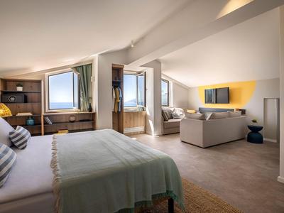 Ruime hotelkamer met twee bedden, tv en zithoek onder schuine plafond.