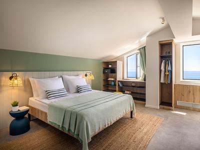 Licht ingericht hotelkamer met tweepersoonsbed, groene accenten en zeezicht.