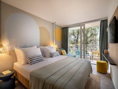 Modern hotelkamer met groot bed, stijlvolle lampen en balkon met uitzicht op bomen.