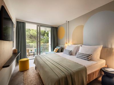 Modern hotelkamer met groot bed, balkon en rustgevend kleurenpalet.