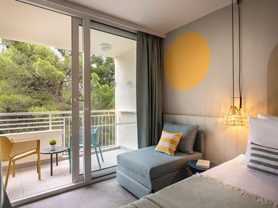 Modern hotelkamer met terras, comfortabele stoel en groot raam met uitzicht op bomen.