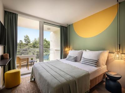 Modern hotelkamer met tweepersoonsbed, balkon en stijlvolle warme wandkleur.