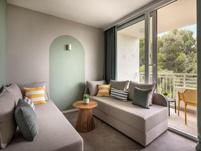 Moderne hotelkamer met zitgelegenheid, balkondeur en uitzicht op bomen.