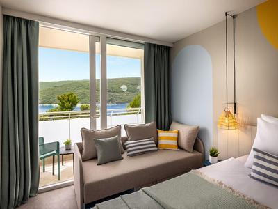 Moderne hotelkamer met bank, bed en uitzicht op terras en natuur.