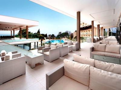 Luxuriöse Terrasse mit weißen Sitzmöbeln und Blick auf Pool und Garten bei klarem Himmel.