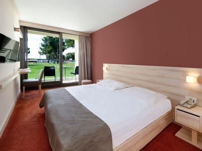 Modern hotel room with double bed, TV on the wall, and view of a terrace with garden.