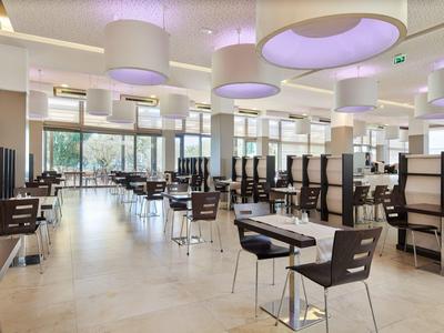 Modern restaurant with wooden chairs, tables, and large ceiling lights in a bright setting.