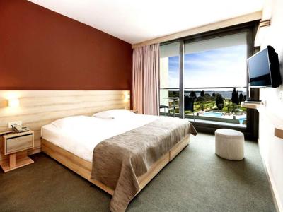 Modern hotel room with large bed, side nightstand, and balcony with sea view.