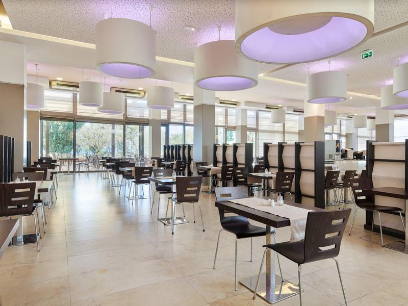 Modern restaurant with wooden chairs, tables, and large ceiling lights in a bright setting.