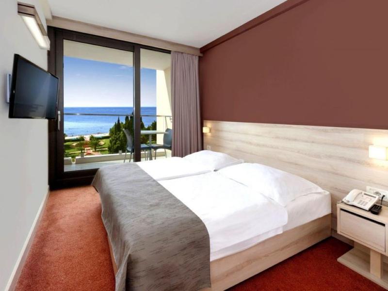 Modern hotel room with double bed, wall-mounted TV, and balcony with sea view.