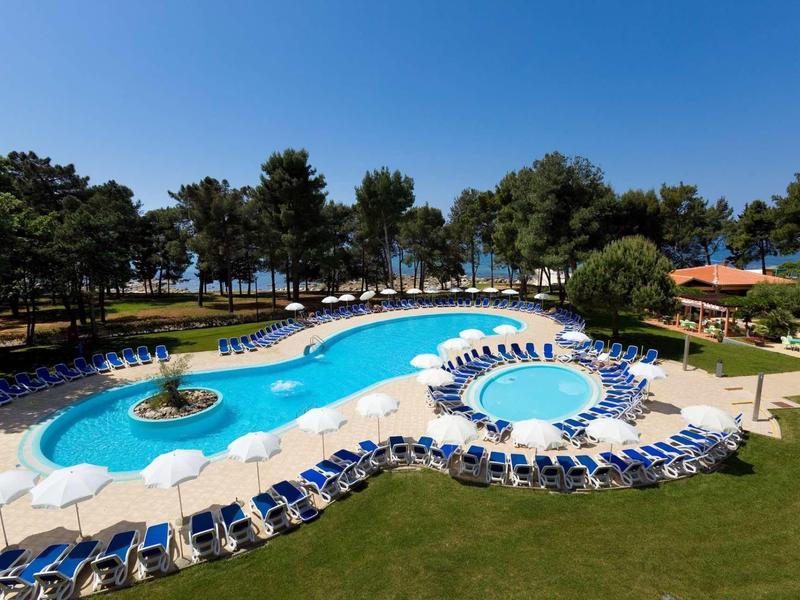 Grand piscine de villégiature avec chaises longues, parasols et arbres sous un ciel clair