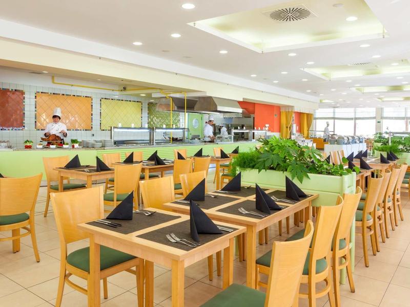 Salle à manger moderne et lumineuse avec tables dressées et chaises vertes dans un hôtel.