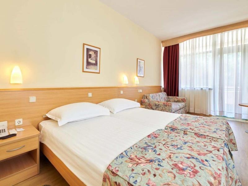 Chambre d'hôtel lumineuse avec lit double, lampes de chevet et balcon avec rideaux.