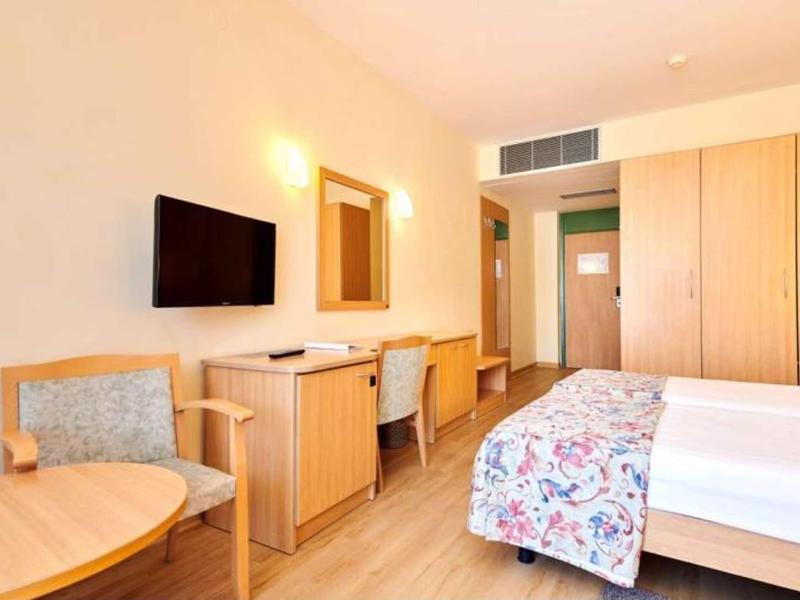 Chambre d'hôtel lumineuse avec lit double, bureau, chaises et télévision à écran plat montée au mur.