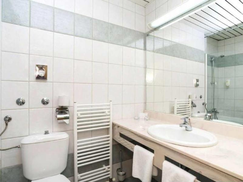 Salle de bain lumineuse avec toilettes, lavabo, grand miroir et murs carrelés blancs.