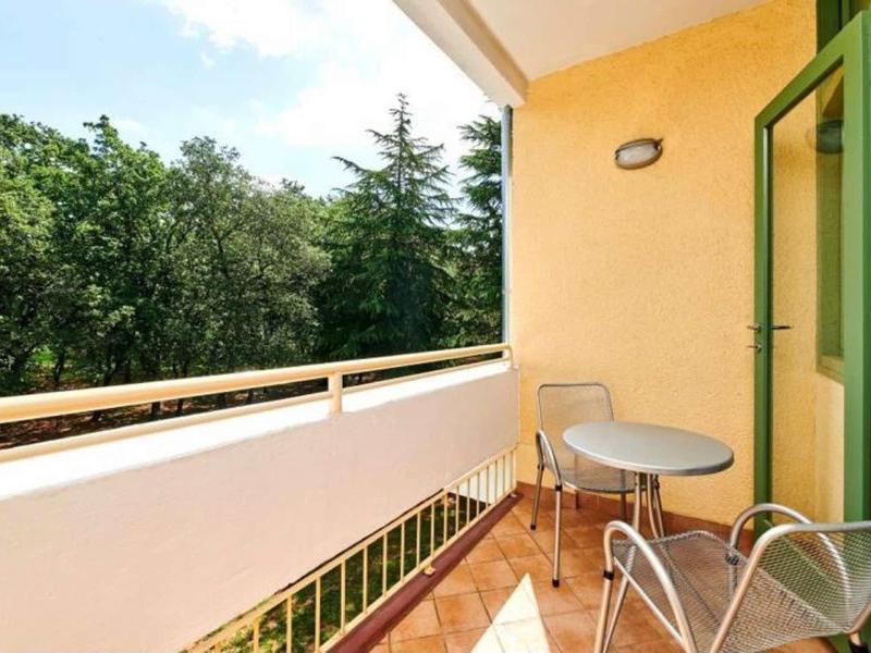 Balcon avec table et chaises, entouré d'arbres verts et d'un mur jaune.