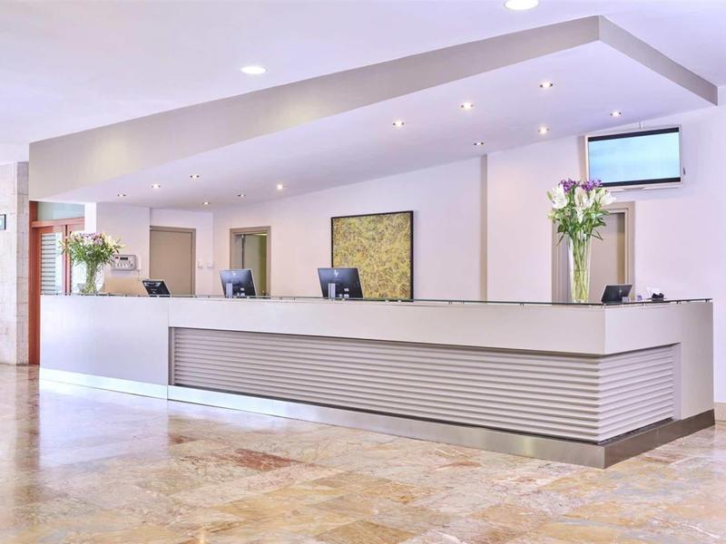 Réception d'hôtel lumineuse avec comptoir moderne et arrangements floraux.