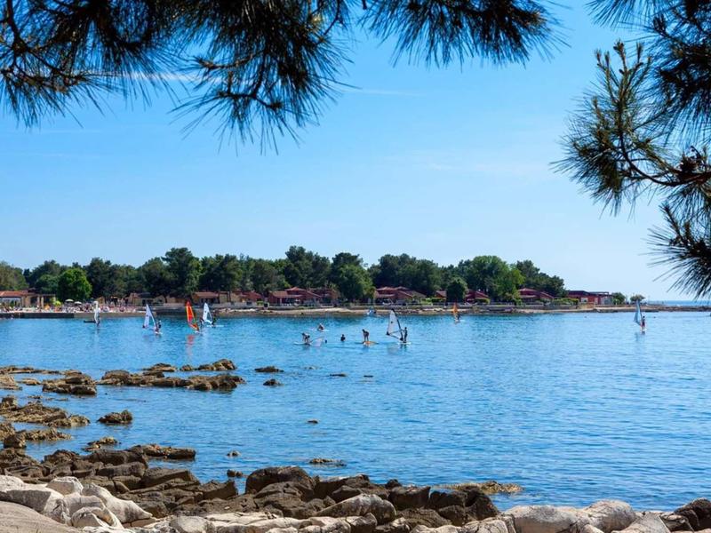 Plage avec rochers et personnes dans l'eau claire, entourée d'arbres et ciel bleu