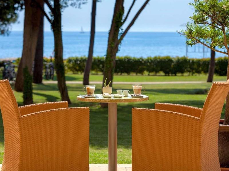 Deux chaises orange autour d'une petite table avec vue sur la mer et un jardin.