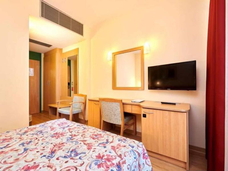 Chambre d'hôtel lumineuse avec un lit, un bureau, une chaise, une télévision et un grand miroir.