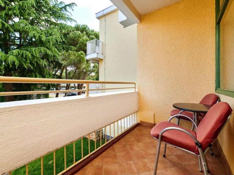 Balcon avec deux chaises rouges donnant sur des arbres à côté d'un bâtiment hôtelier.