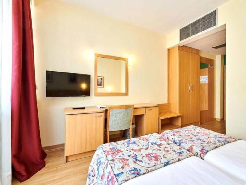 Chambre d'hôtel lumineuse avec lit double, bureau, télévision et rideau rouge.