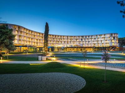 Modern hotel with curved facade and illuminated pool at night.