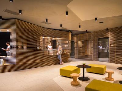 Modern hotel lobby with wood paneling, yellow seating, and round tables.