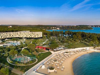 Hotel complex on the beach with pools, sunshades, and wooded surroundings along the coast.