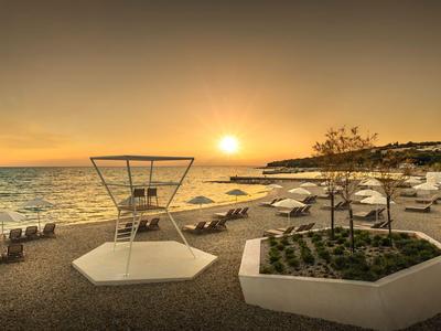 Sunset at the beach with lounge chairs and umbrellas by calm sea.