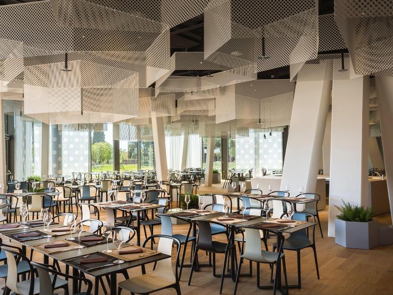 Großer, moderner Gastraum mit Holztischen, Metallstühlen und dekorativem weißen Deckensegel.