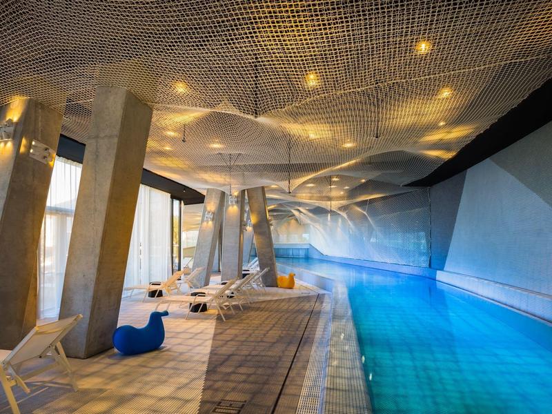 Moderner Innenpool mit blauem Wasser, weißen Liegestühlen und einzigartiger gewellter Decke.