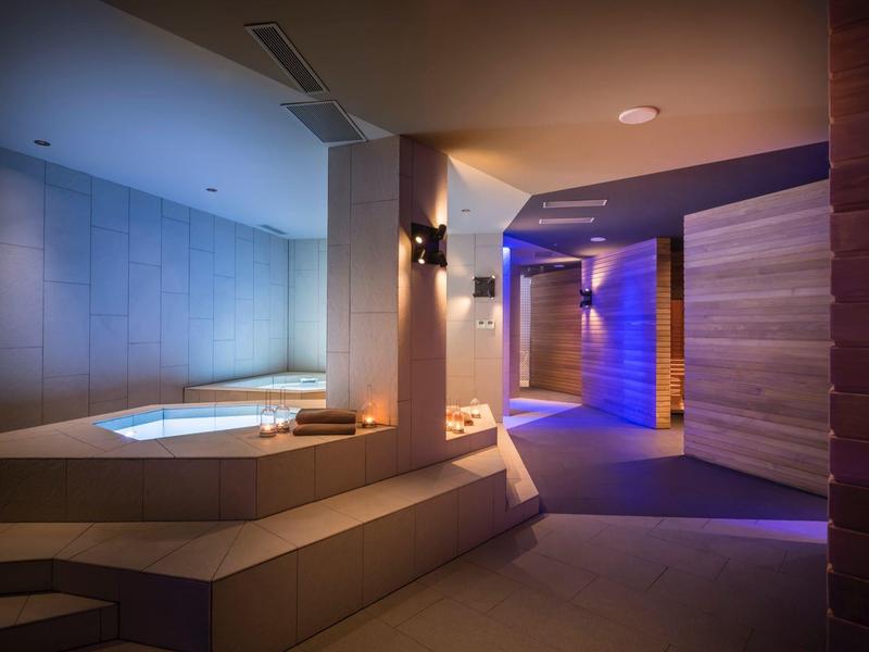 Moderner Wellnessbereich mit beleuchtetem Whirlpool, blauen Lichtern und holzverkleideten Wänden.