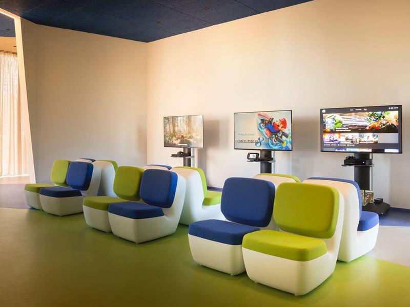 Moderner Raum mit farbenfrohen, gepolsterten Sitzgelegenheiten und zwei Monitoren an der Wand.