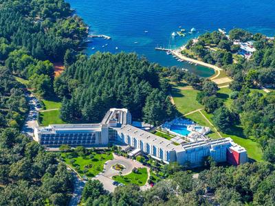 Grande hotel con piscina circondato da foresta sulla costa con vista sul mare blu.