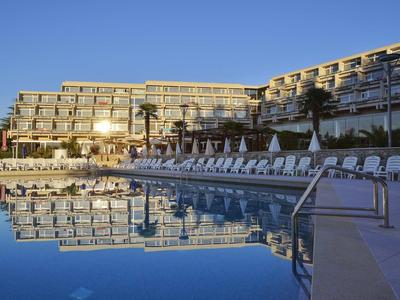 Grande hotel con numerose sdraio e una grande piscina sotto un cielo limpido.