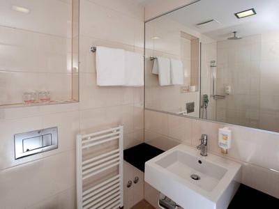 Modern hotelbadkamer met grote spiegelwand, witte wastafel en handdoeken.